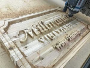 A cnc router carving a wooden sign.