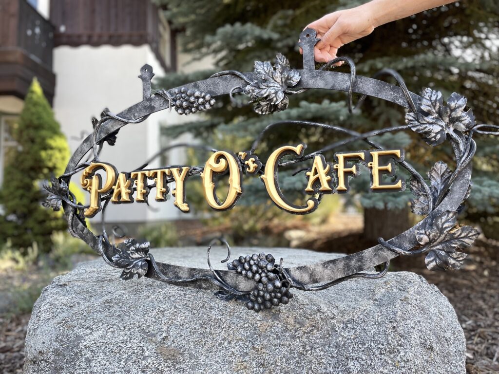 Metal Sign with scroll details and prismatic gold leaf letters.